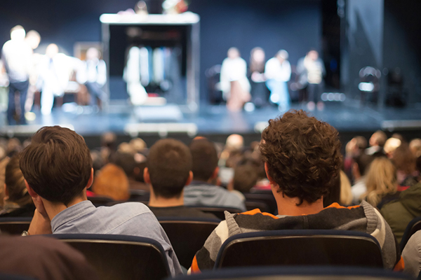 people sitting in audience watching performers on stage