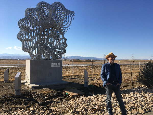 artist stands in front of large shell-shaped sculpture