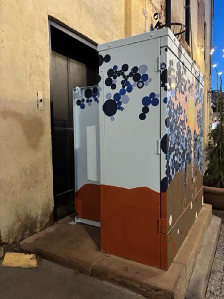 North side of cabinet mural in progress with tan wall with doorway behind and strip of blue sky in background