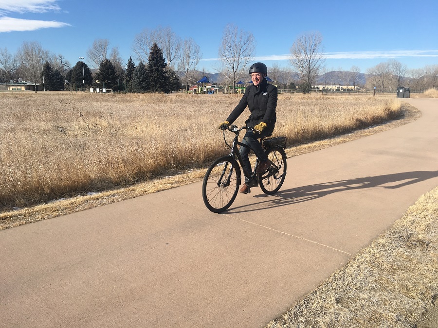 Person rides their class 1 e-bike on a paved multi-use trail...with a smile.