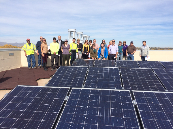 A group of people standing behind rooftop solar panels