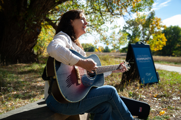 Liz Barnez playing guitar along the Poudre Trail at Lee Martinez Park