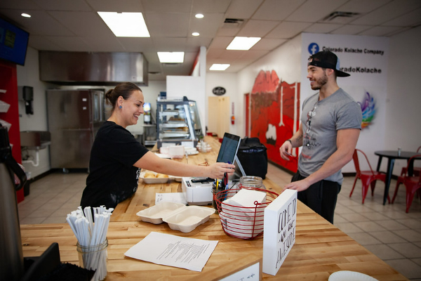 Photo of a cashier and customer in a small restaurant. Both look happy.