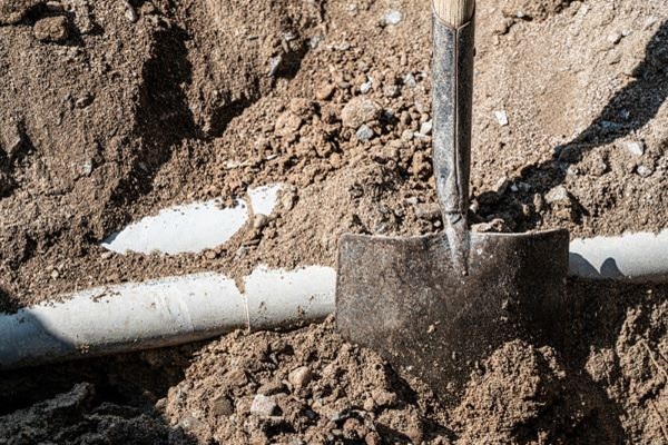 A shovel and white water line pipe surrounded by dirt.