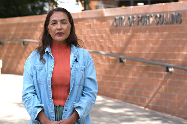 woman with dark hair and denim shirt standing in front of brick ramp to Fort Collins City Hall