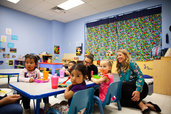Niños y maestros sentados en una mesa en un salón de clases de educación temprana.
