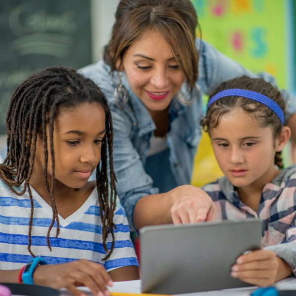 An adult pointing at a screen that two children are looking at attentively