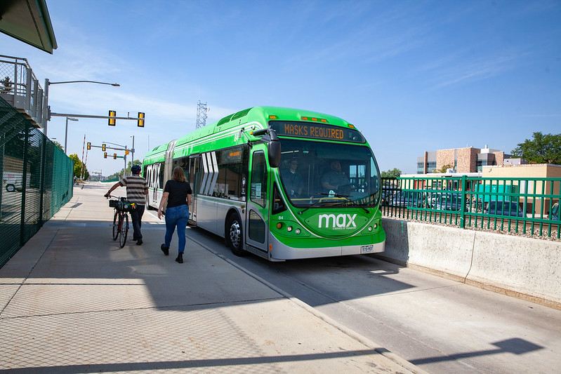 People walk, one with a bicycle, on the Mason Trail as the Max bus drives by.