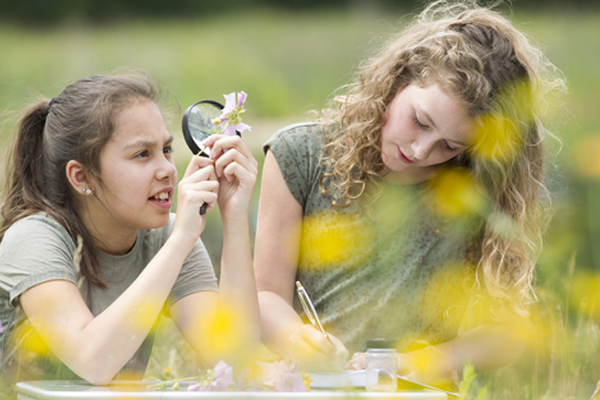 two young girls looking at flowers with a magnifying glass