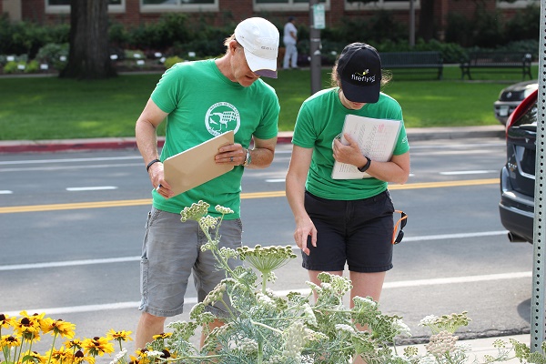 Two individuals wearing green shirts and holding clipboards observing flowers