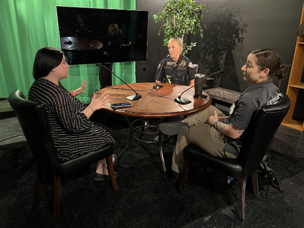 three women, including one in a police uniform, sitting around a round table having a discussion