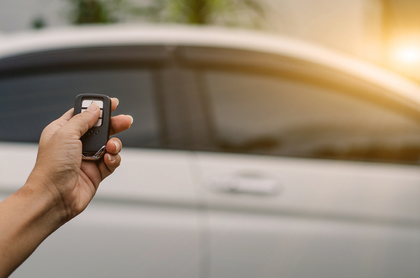 Hand holding a vehicle fob and electronically locking of a white car