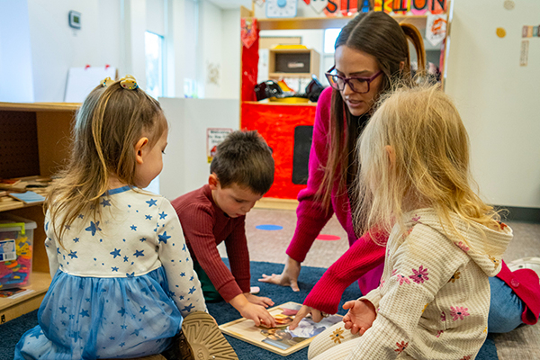 A photo of a group of children and one adult sitting and playing.