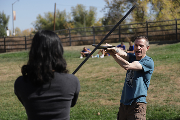 A photo of two people practicing sword fighting with training swords.