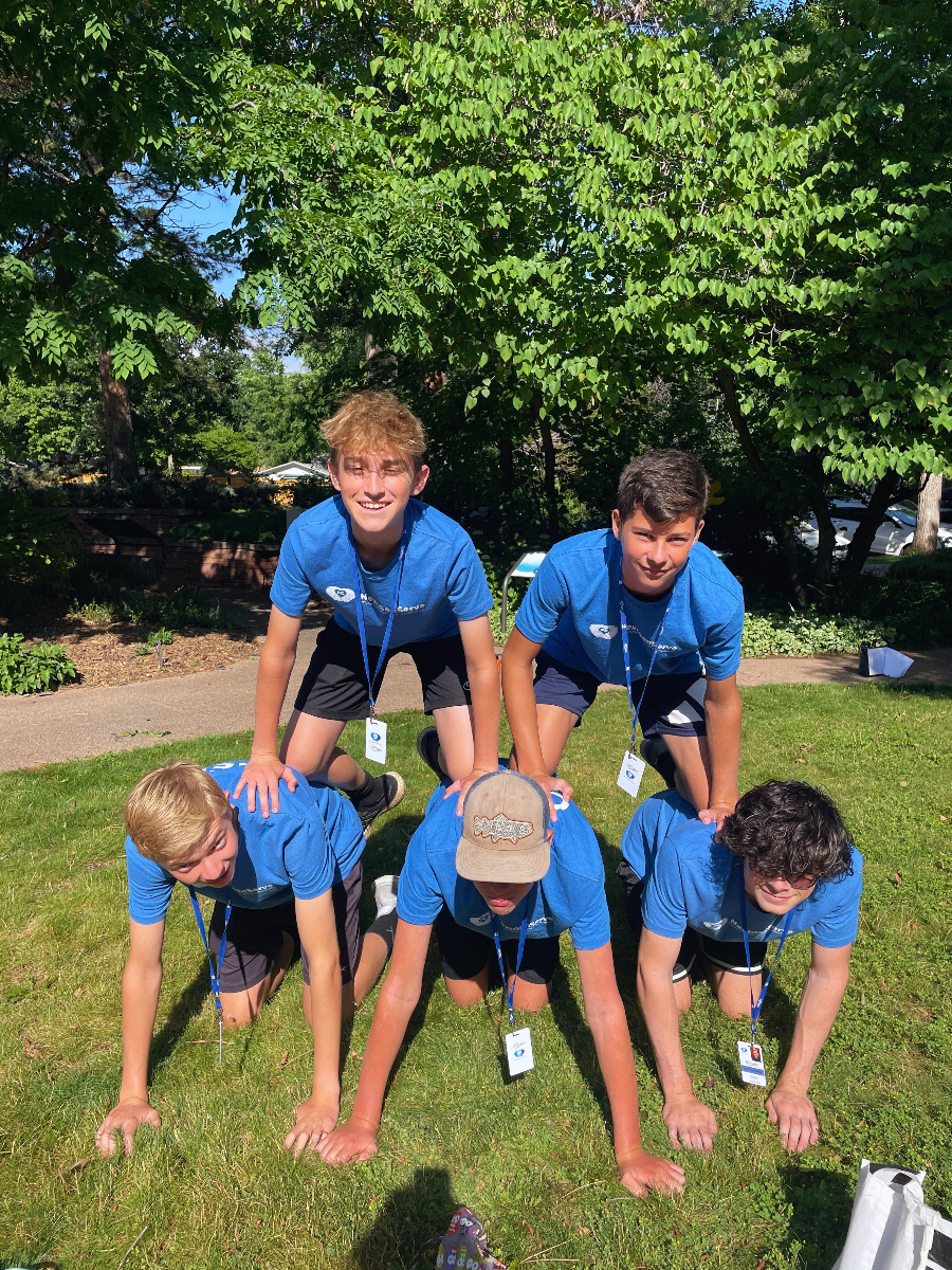 5 boys creating a human pyramid in the grass.